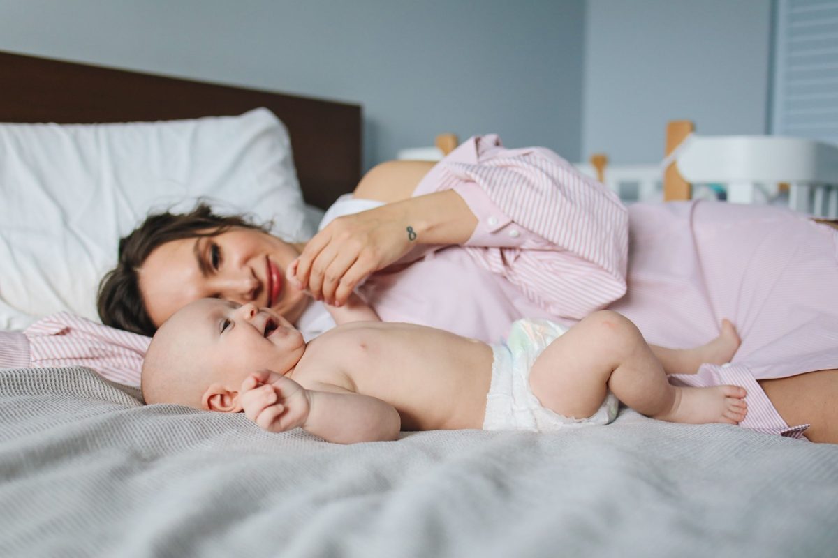 Mother and smiling baby lying together on a bed